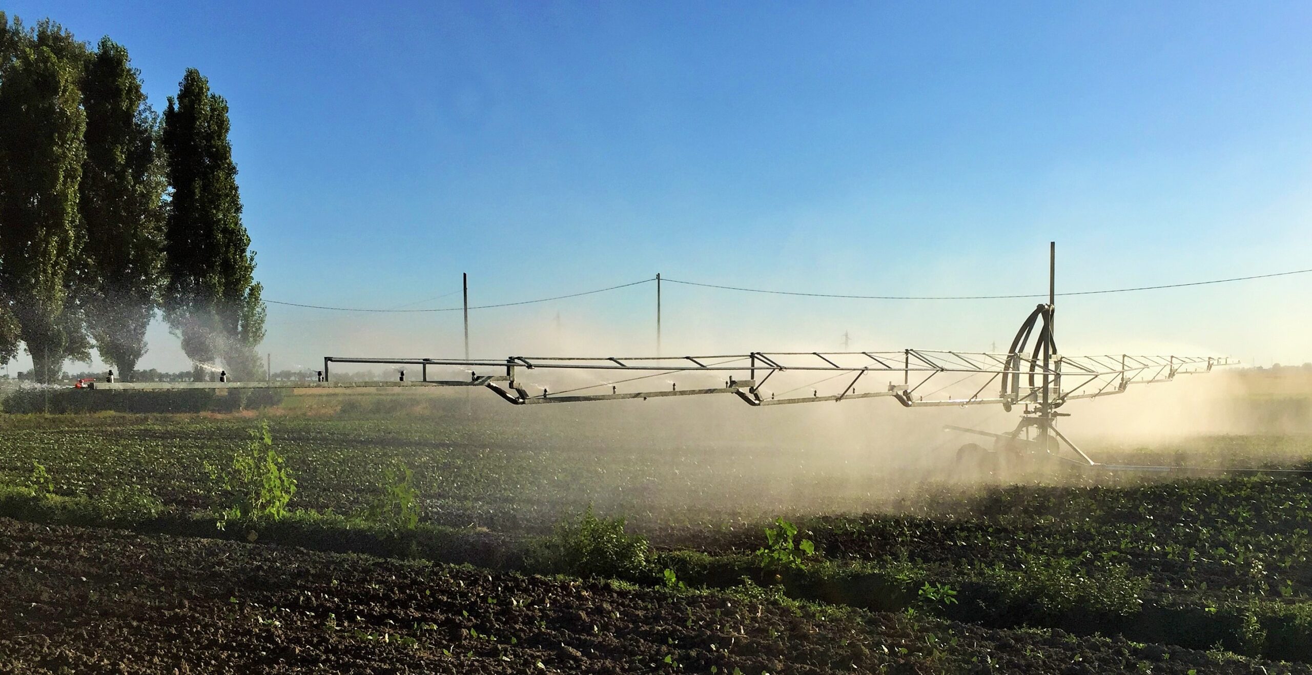 Un'ala piovana in azione in un campo composta un braccio d'acciaio di diversi metri supportata da un carrello in fase di irrigazione.